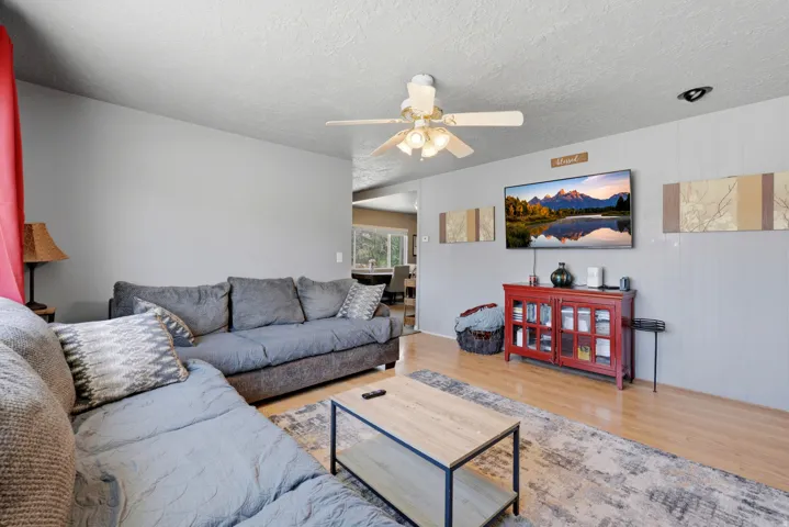 Living area featuring wood-finish flooring, a ceiling fan with integrated lighting, and light grey walls