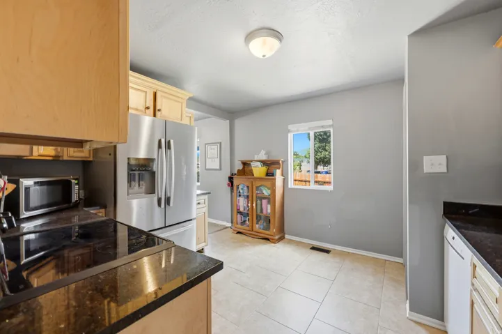 Kitchen featuring stainless steel appliances, light wood cabinetry, dark countertops, and tile flooring