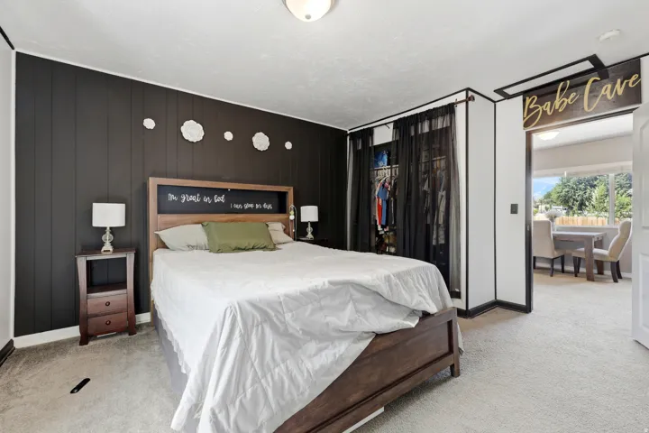 Carpeted interior with a dark paneled accent wall, wood-finish bed frame, and built-in closet with dark drapery