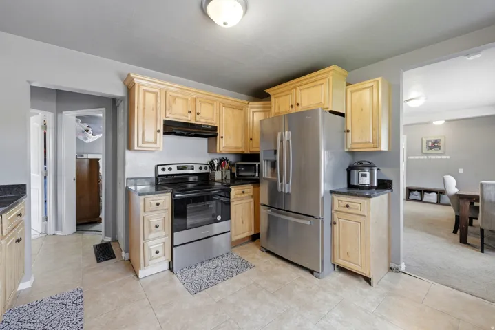 Kitchen featuring warm wood cabinetry, dark countertops, a stainless steel refrigerator, and a stainless steel range with overhead ventilation