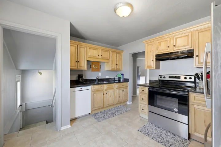 Kitchen featuring light wood cabinetry, dark countertops, a stainless steel electric range, and a white dishwasher