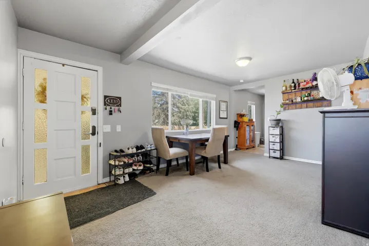 Entryway and dining space featuring a paneled entry door with frosted glass accents, exposed ceiling beams, a large picture window, and neutral carpeting throughout