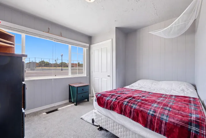 Bedroom featuring a wide window with white blinds, grey wainscoting, and carpet flooring