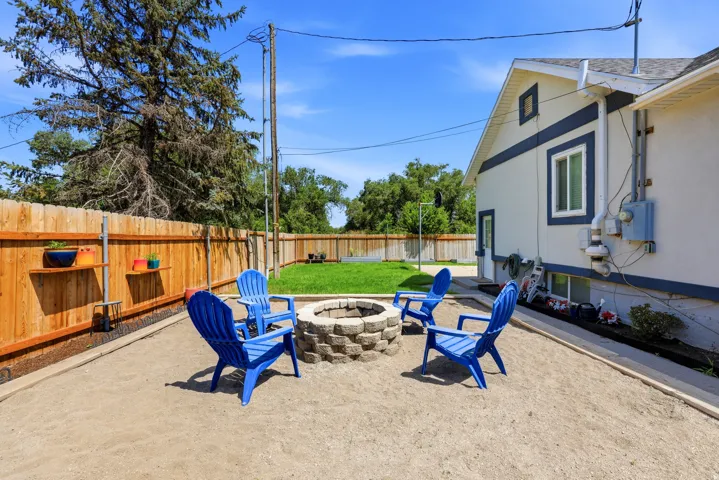 Backyard featuring a stone fire pit, gravel patio area, wooden privacy fence with shelving, and a manicured lawn space