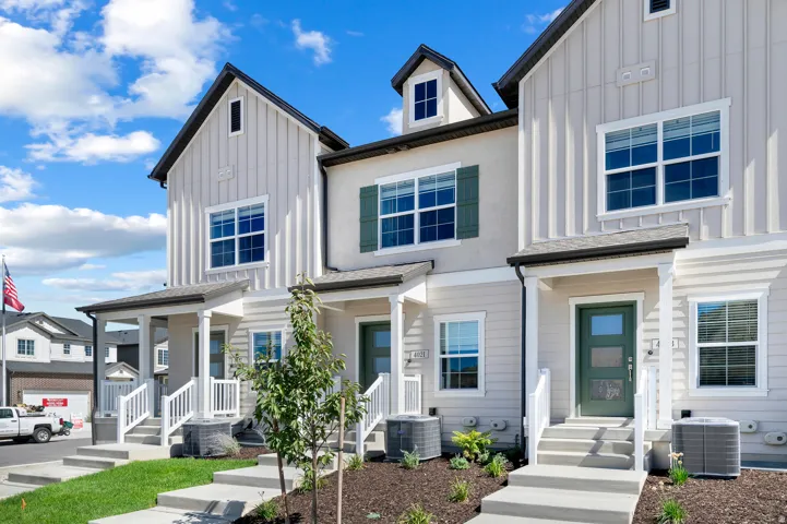 Contemporary townhome exterior featuring vertical siding, stucco accents, dark green shutters, a covered porch, and concrete steps