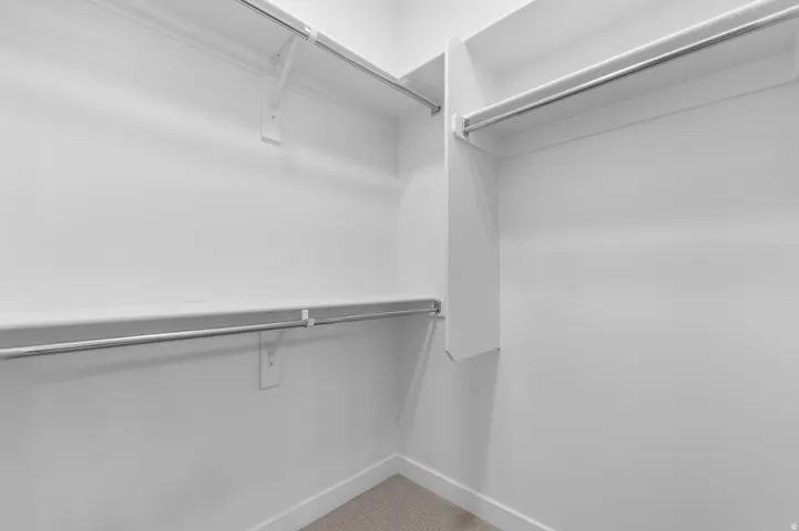 Walk-in closet featuring white shelving, multiple hanging rods, and neutral-toned carpeting