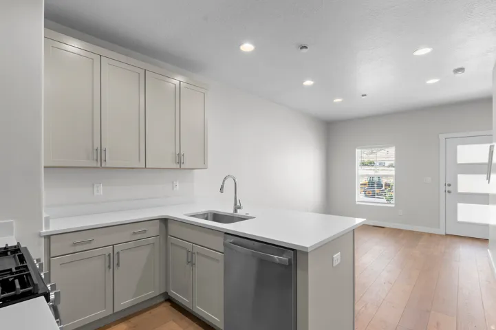 Recessed lighting illuminates the kitchen featuring light-toned cabinetry, light countertops, and a stainless steel sink with a gooseneck faucet
