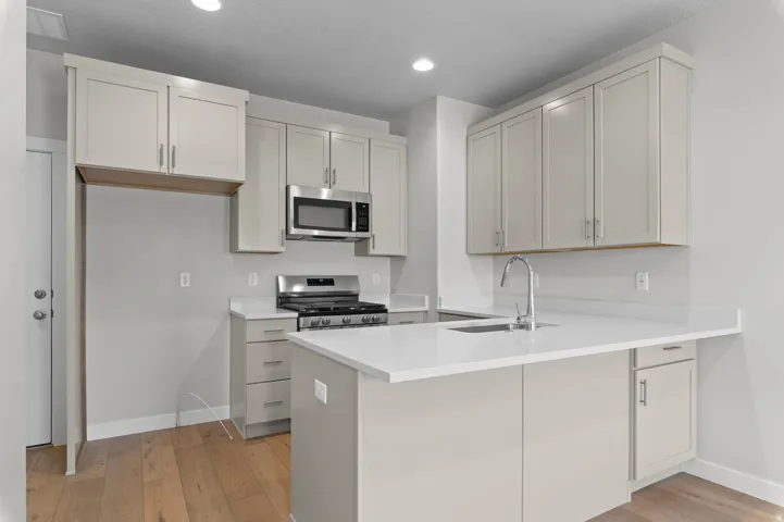 Kitchen featuring light-toned cabinetry, stainless steel microwave and range, wood-finish flooring, and light-toned countertops