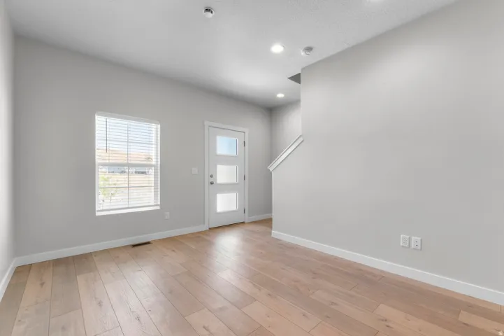 Hardwood-finish flooring, recessed ceiling lighting, a modern entry door with frosted glass panels, and a window with blinds