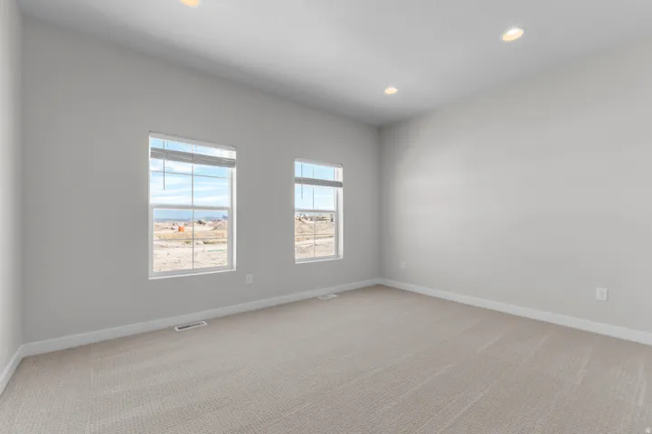Recessed ceiling lighting, two windows with blinds, light-toned carpet, and neutral wall tones