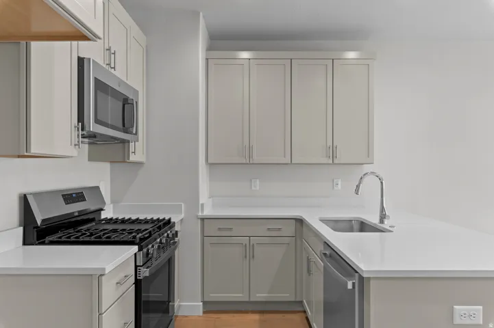 Kitchen featuring light-toned cabinetry, stainless steel appliances, solid surface countertops, a stainless steel sink, and wood-finish flooring