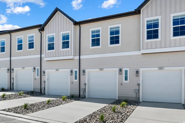 Exterior featuring stucco and horizontal siding, multiple single-car garages, white-framed windows, and decorative exterior lighting