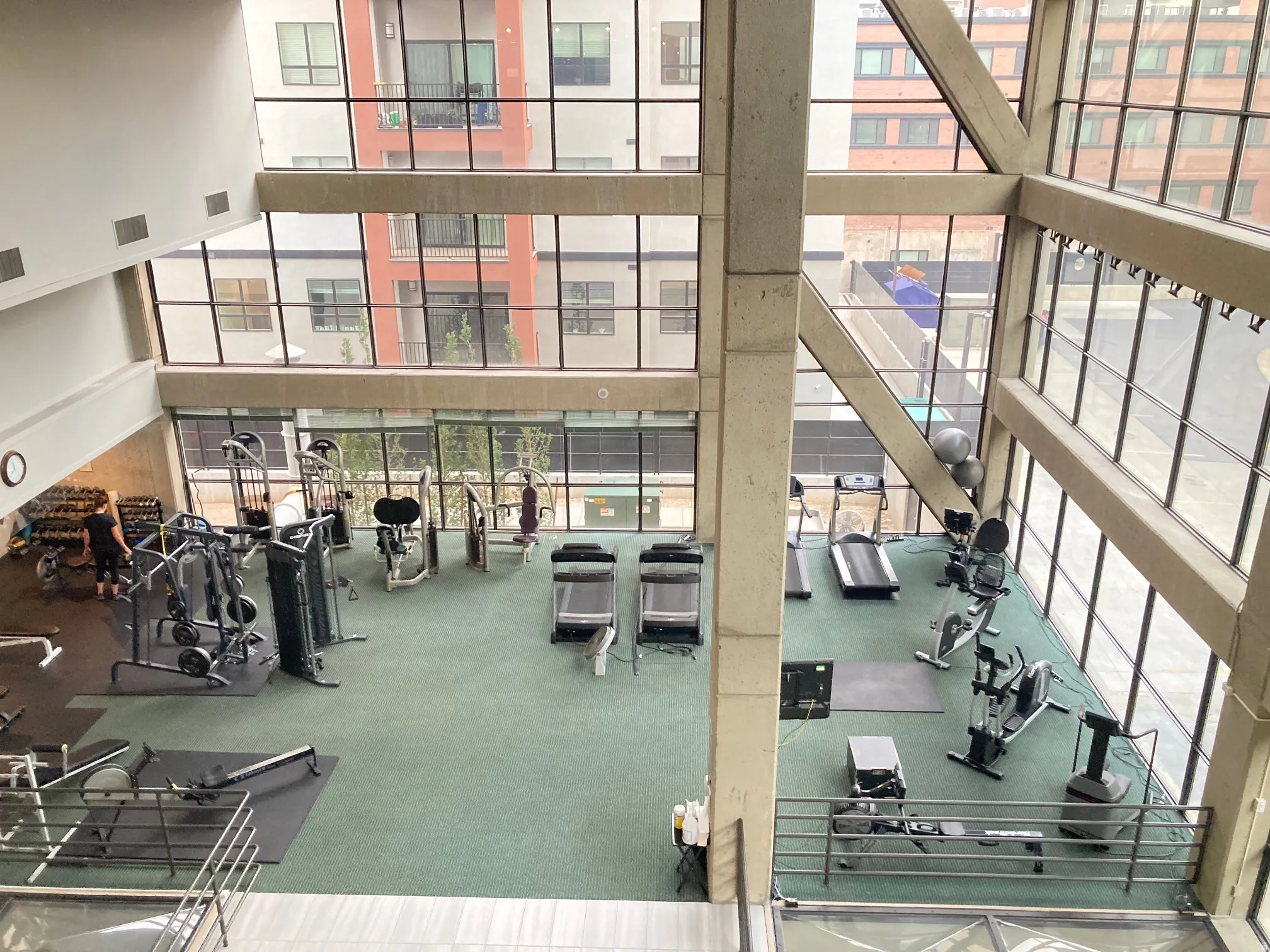 Two-story fitness facility featuring a variety of cardio equipment, strength training machines, free weights, and a designated mat area, all set against a backdrop of expansive floor-to-ceiling windows