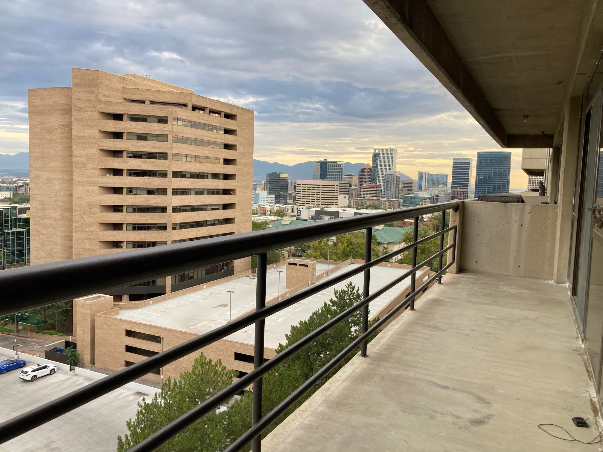 Expansive concrete balcony featuring a black metal railing and urban skyline backdrop