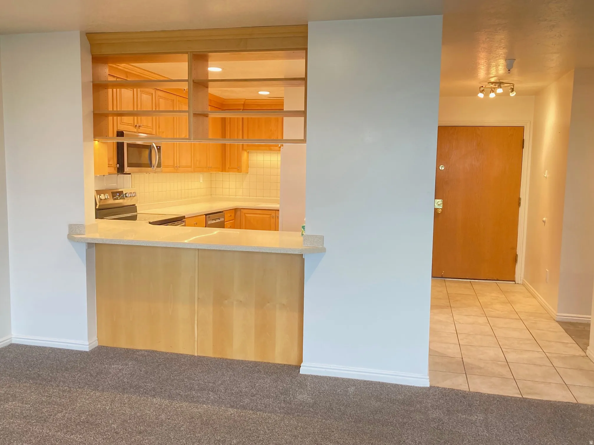 Kitchen pass-through with a light wood-finish breakfast bar, light countertops, and built-in shelving