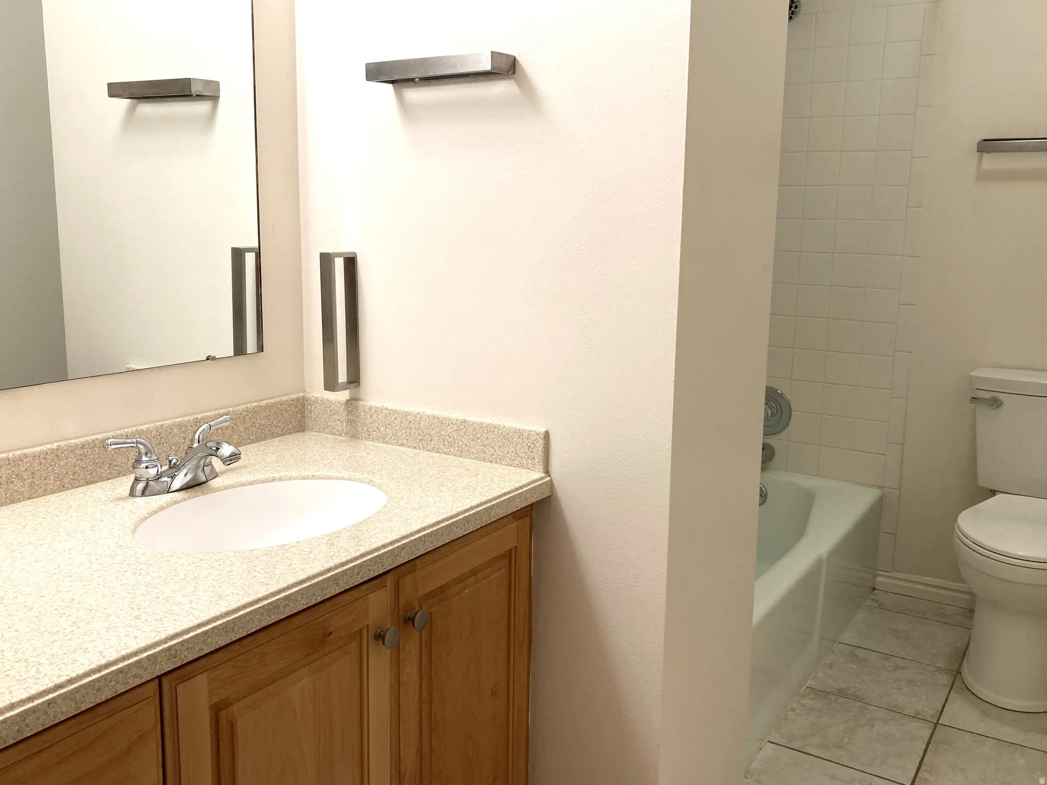 Bathroom featuring a wooden vanity with a speckled countertop, an integrated sink, a chrome faucet, and a large wall mirror