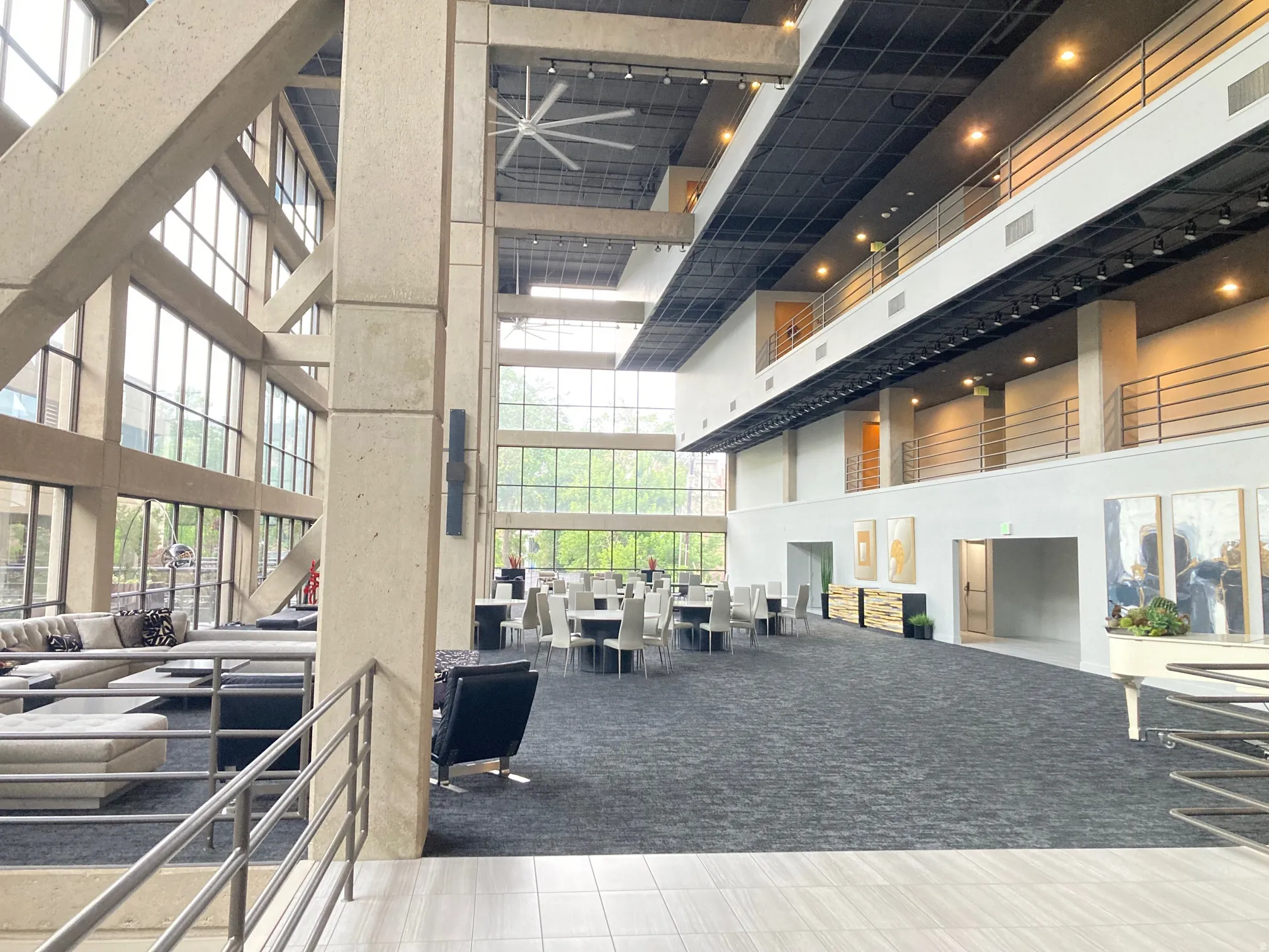 Spacious multi-level interior featuring extensive window walls, textured dark carpet flooring, and a large ceiling fan