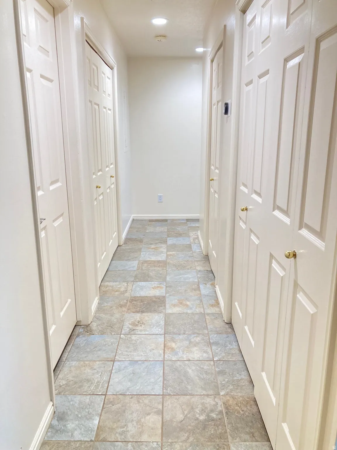 Hallway featuring square-format tile flooring, recessed lighting, and multiple paneled doors with brass-finish hardware