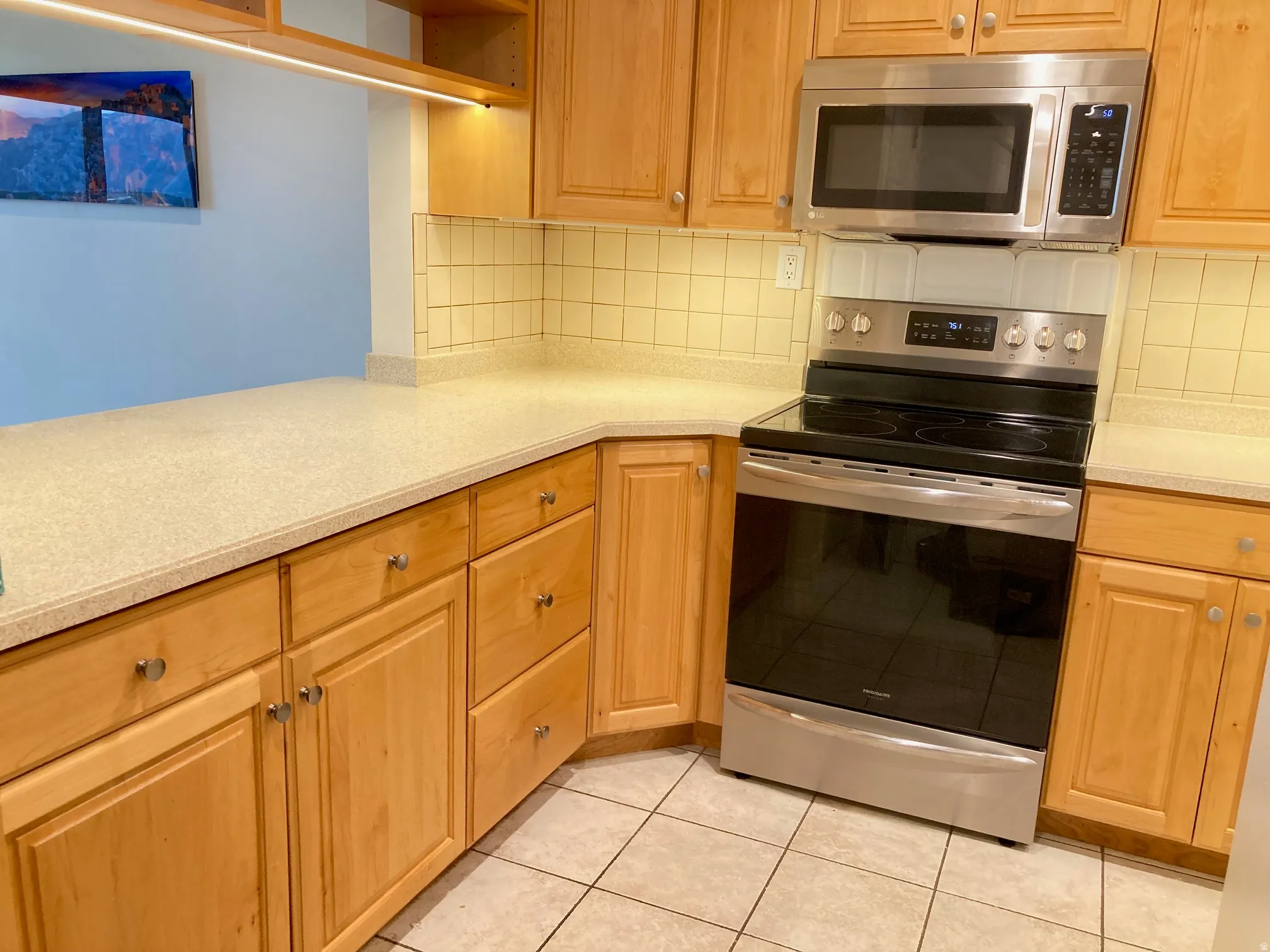 Kitchen featuring natural wood cabinetry, light-colored countertops, a tile backsplash, and stainless steel appliances including a range and microwave
