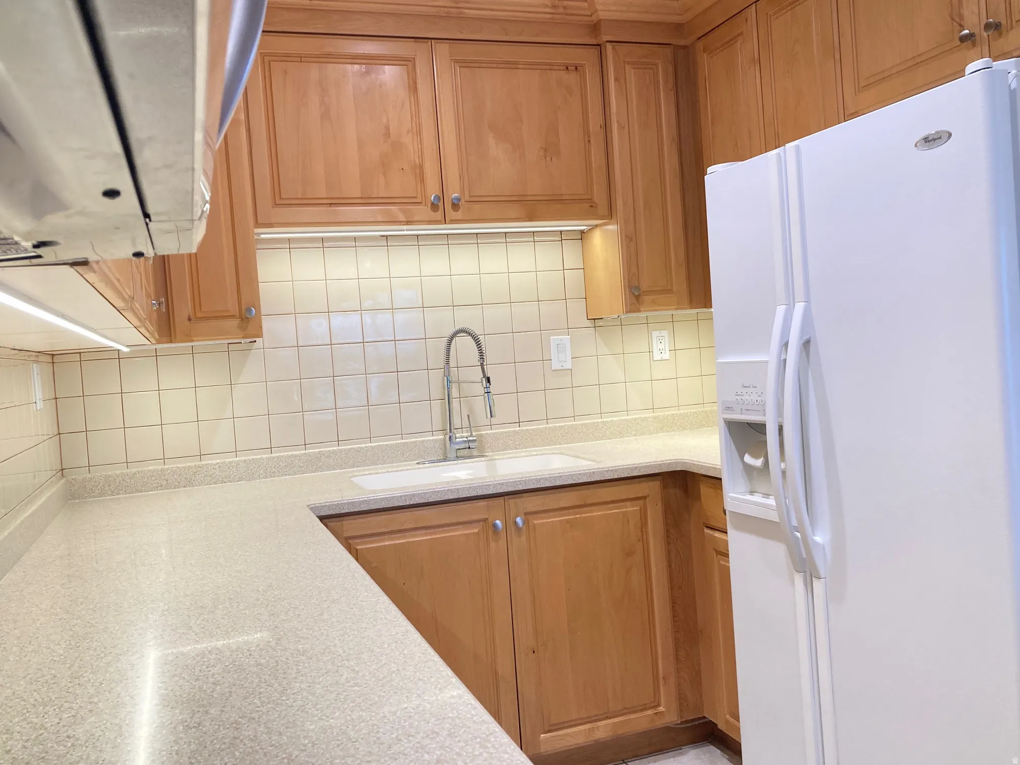 Kitchen featuring warm-toned cabinetry, light-toned countertops, and a white tile backsplash