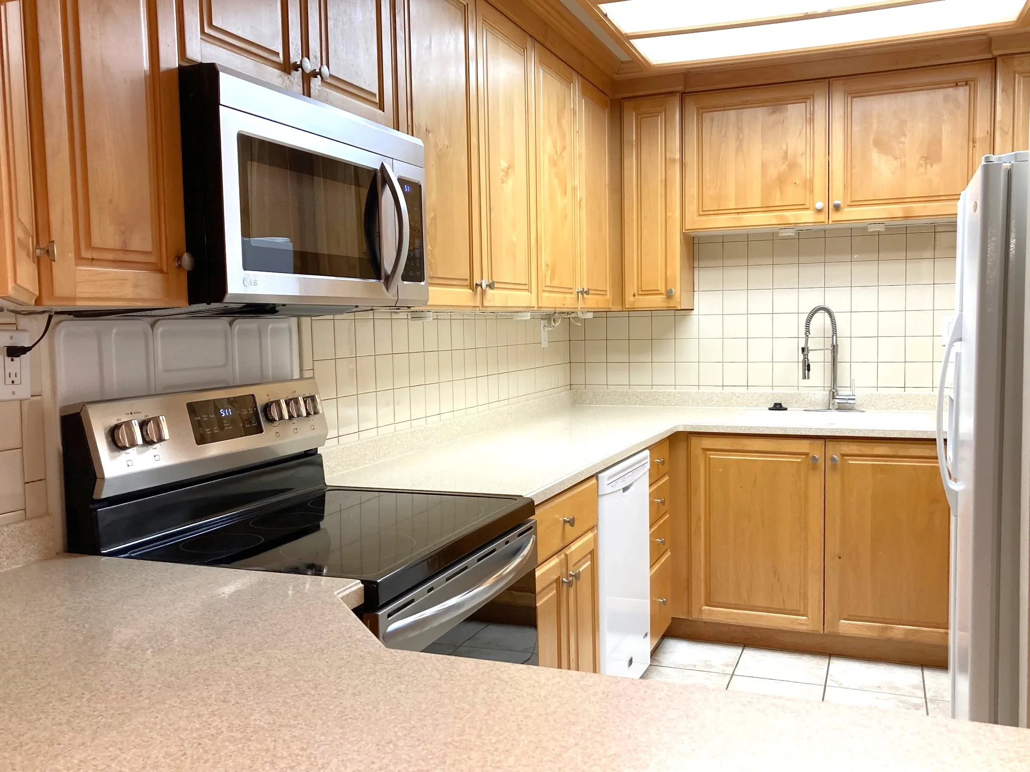 Kitchen featuring wood cabinetry, light countertops, and a white square tile backsplash