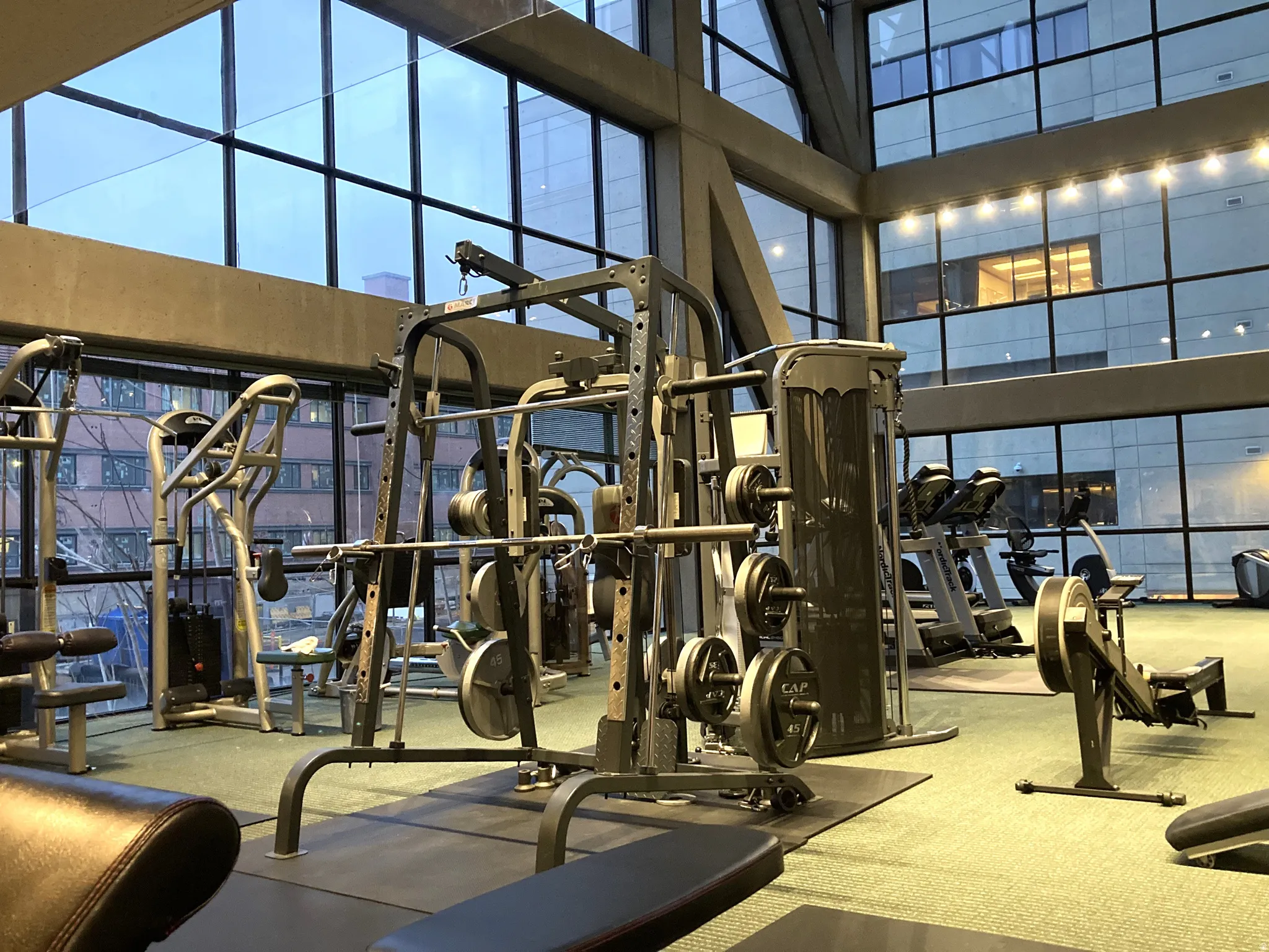 Fitness center featuring extensive full-height windows, a variety of exercise equipment including weights and cardio machines, structural steel beams, and recessed lighting