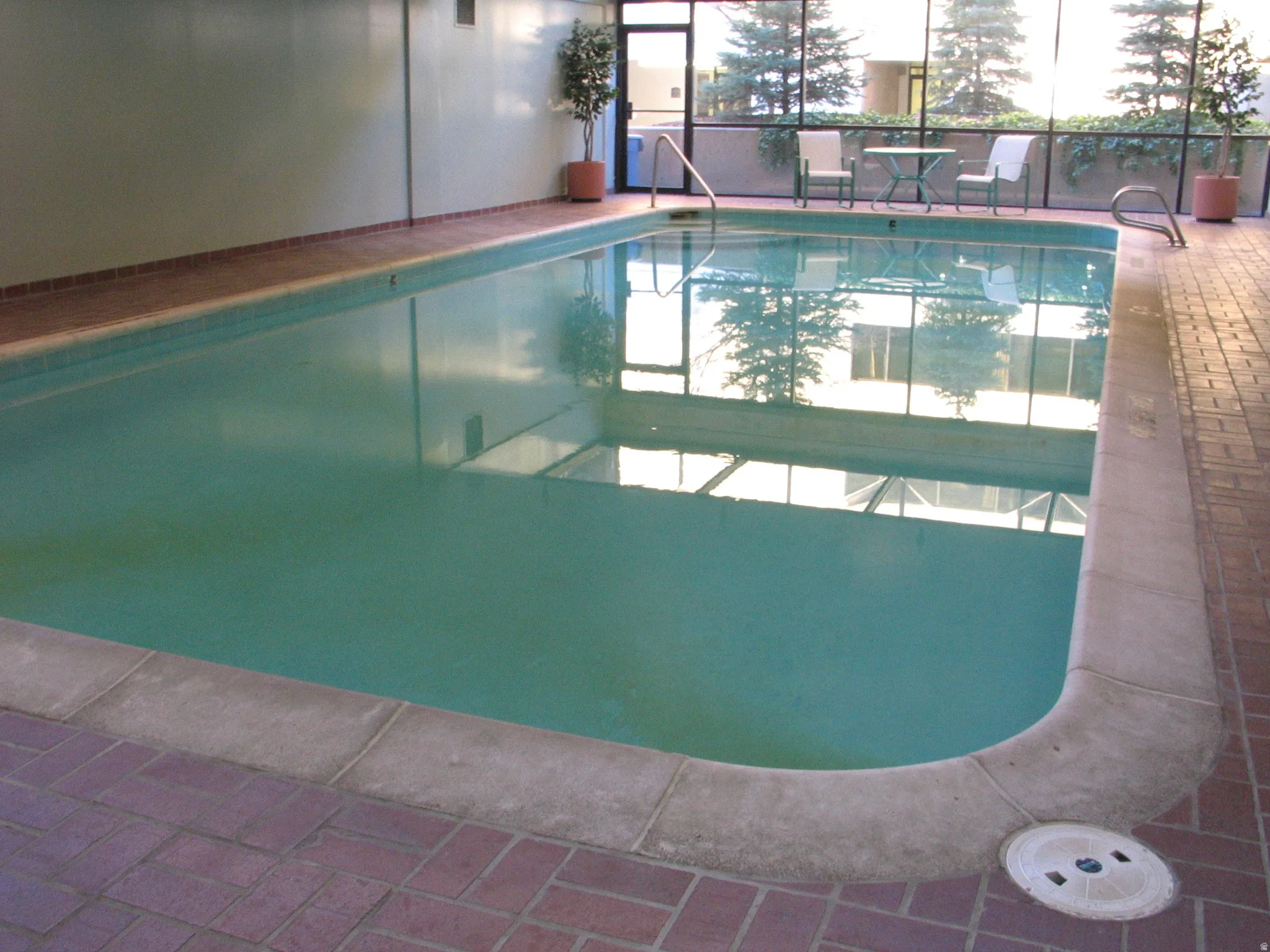 Indoor swimming pool featuring a brick-patterned tile surround and direct access to an outdoor patio with clear panel fencing