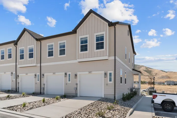 Townhome exterior featuring light-colored siding, a dark roof, individual garage doors, and an outdoor porch