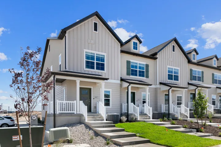 Contemporary townhome exterior featuring board and batten siding, multiple gables, a covered front porch, and concrete steps