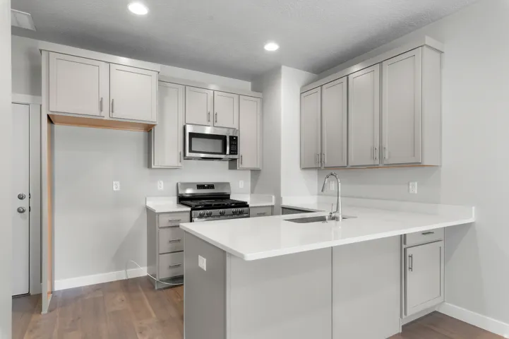 Kitchen featuring wood-finish flooring, light grey cabinetry, stainless steel appliances, white countertops, and recessed lighting
