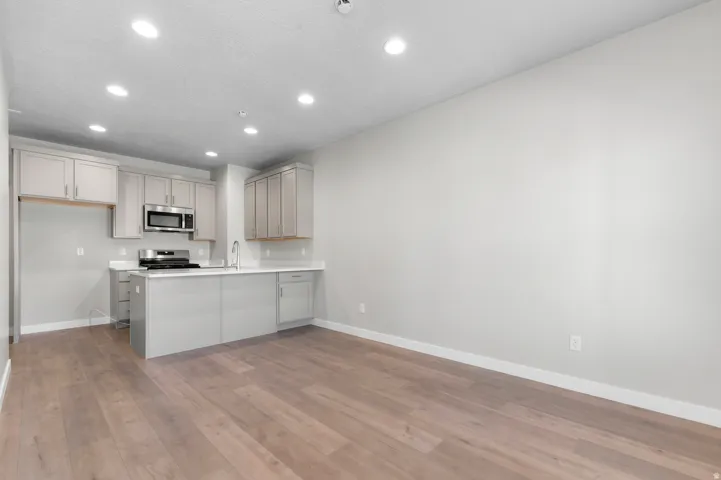Modern kitchen featuring light cabinetry, stainless steel appliances, a center island with sink, and light wood-finish flooring