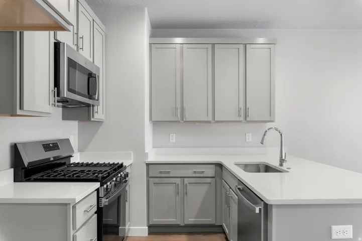 Light gray cabinetry, stainless steel appliances, white countertops, built-in microwave, and a stainless steel sink