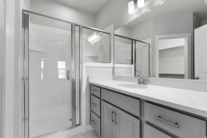 Walk-in shower with clear glass enclosure, expansive vanity with light-toned countertop, integrated sink, and gray cabinetry with drawer pulls