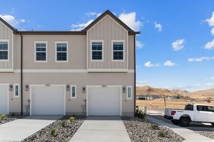 Contemporary townhouse exterior featuring a two-car garage, vertical siding accents, stucco finish, and exterior wall-mounted lighting fixtures