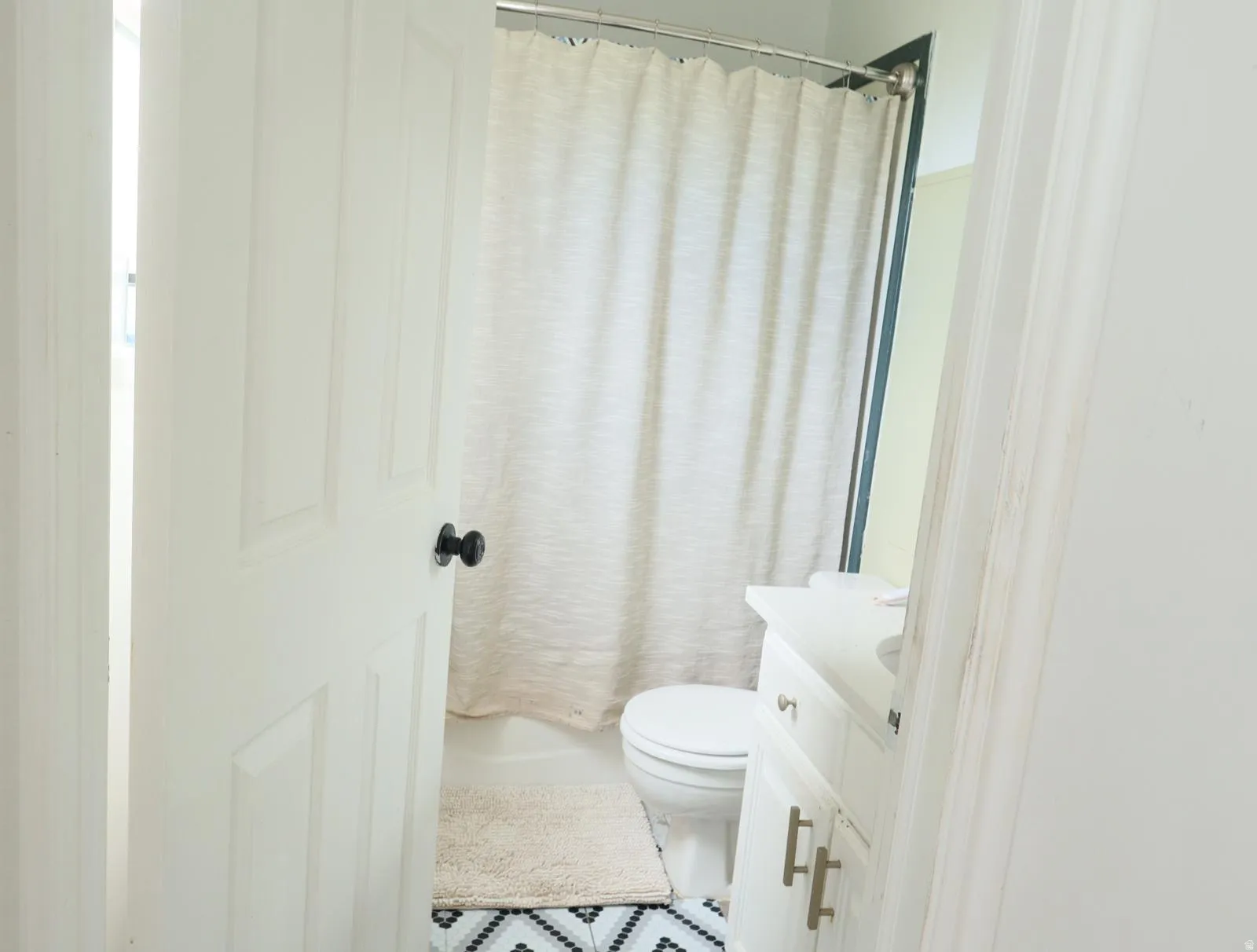 Bathroom featuring a white vanity with cabinet storage, a white toilet, and a shower/tub combination with a light-colored shower curtain