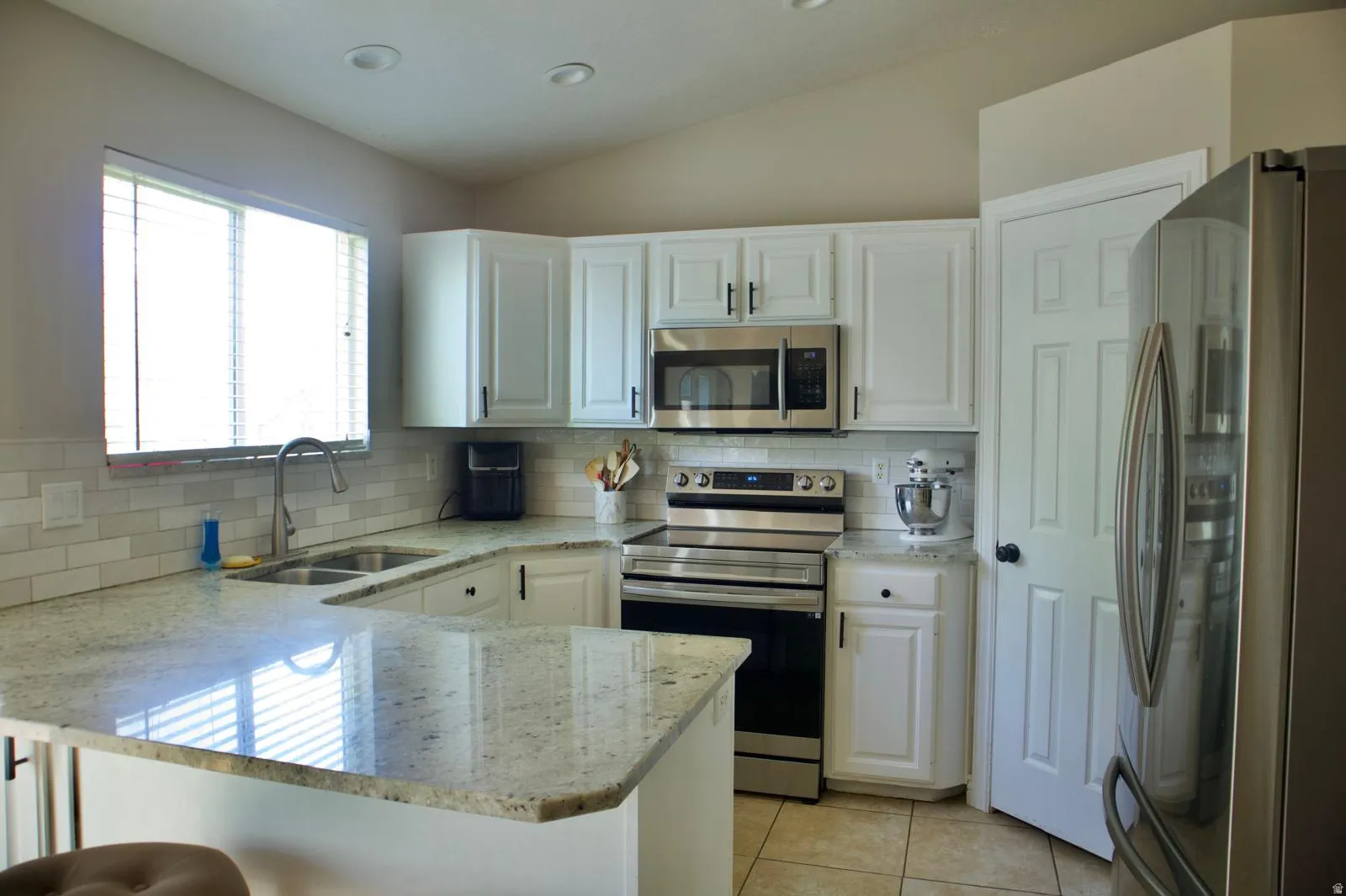 Kitchen featuring white cabinetry, light-toned granite-style countertops, stainless steel appliances, a subway tile backsplash, and a double basin sink