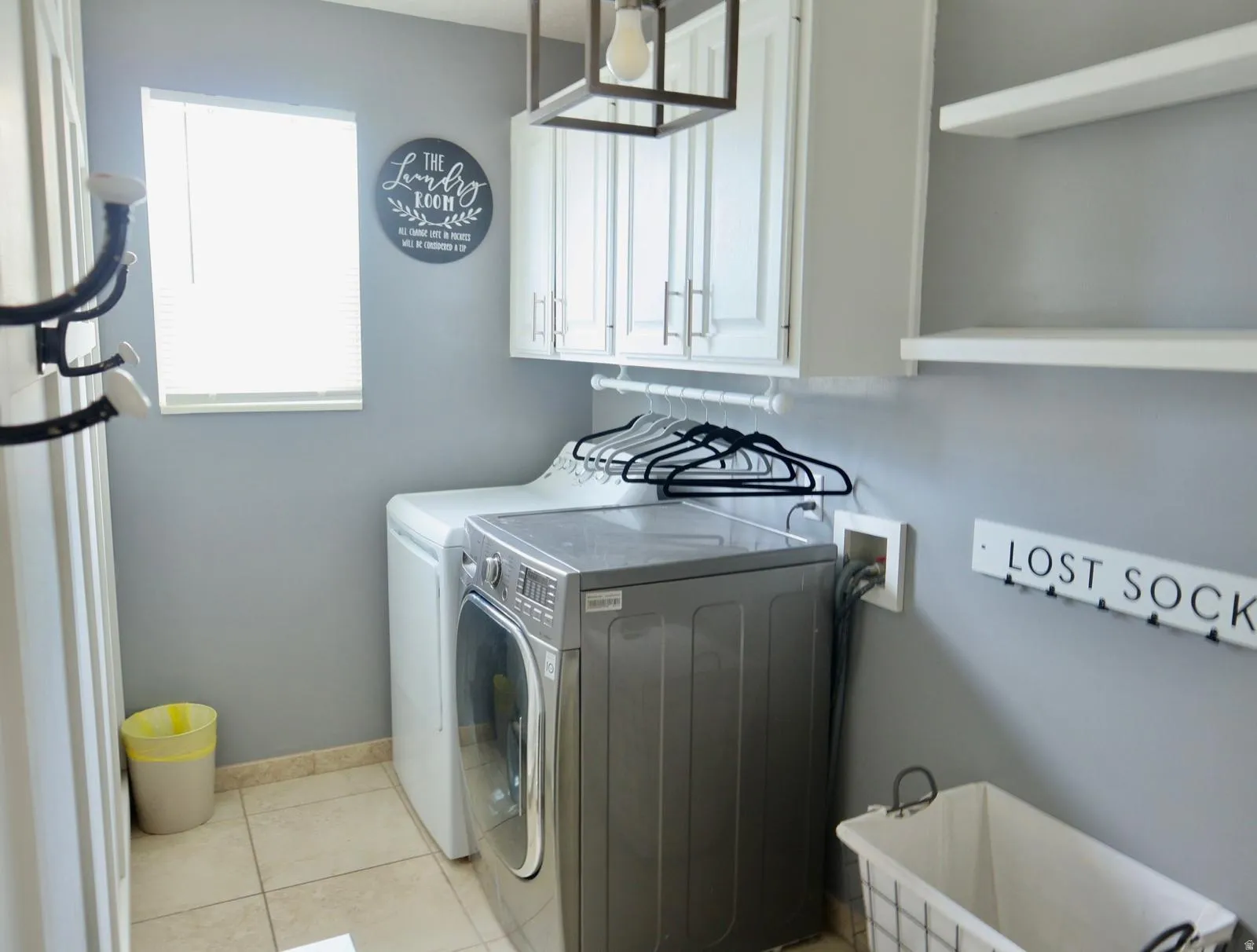 Dedicated utility space featuring tile flooring, white cabinetry with silver hardware, open shelving, and a window for natural light