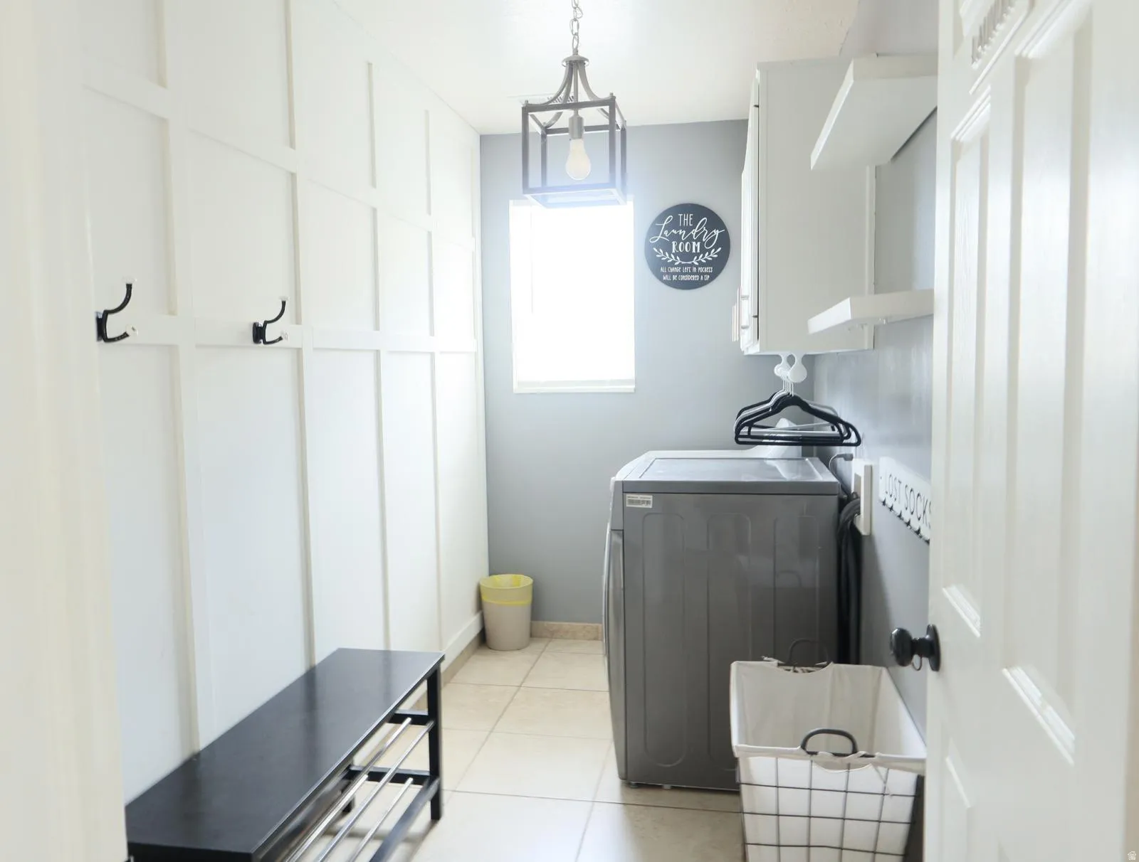 Laundry area with board and batten accent wall, neutral tile flooring, and a single window for natural light