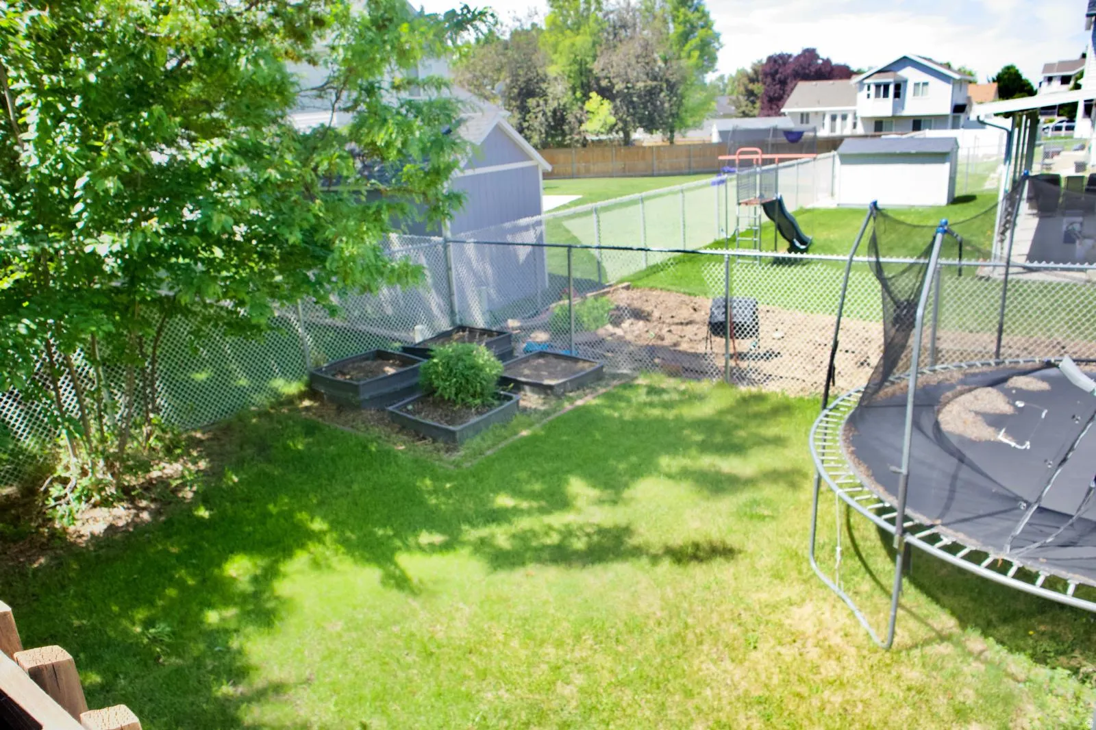 Expansive lawn area featuring a chain-link fence, mature trees, and raised garden beds