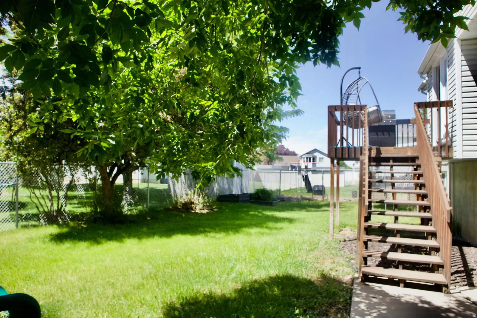 Spacious backyard featuring a large green lawn, mature trees, and a wooden deck with stairs providing outdoor access