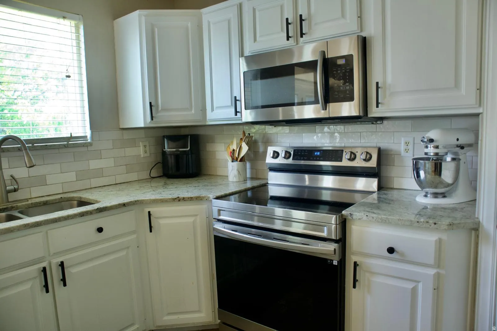Kitchen featuring white cabinetry with matte black hardware, stainless steel appliances, granite countertops, and a subway tile backsplash