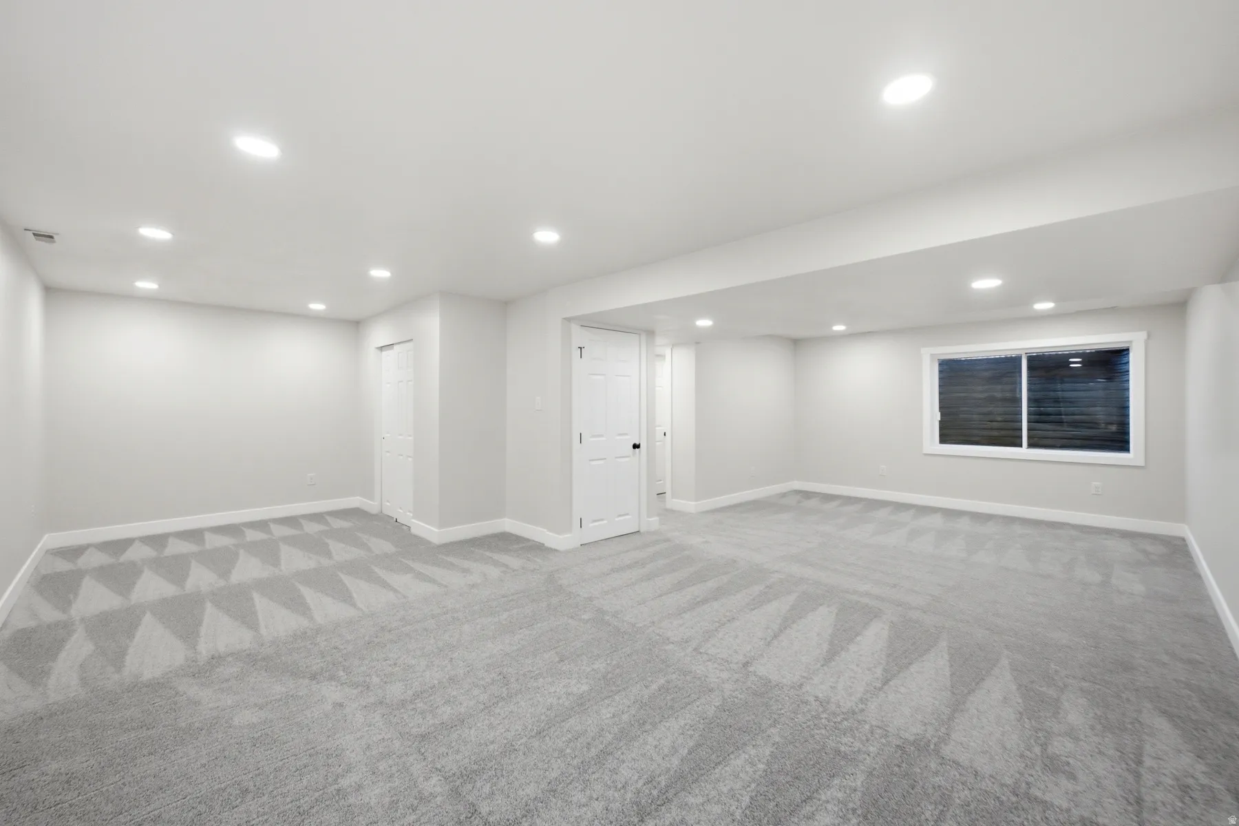 Spacious room featuring light gray walls, recessed lighting, gray patterned carpet, white trim, and a horizontal window with white framing