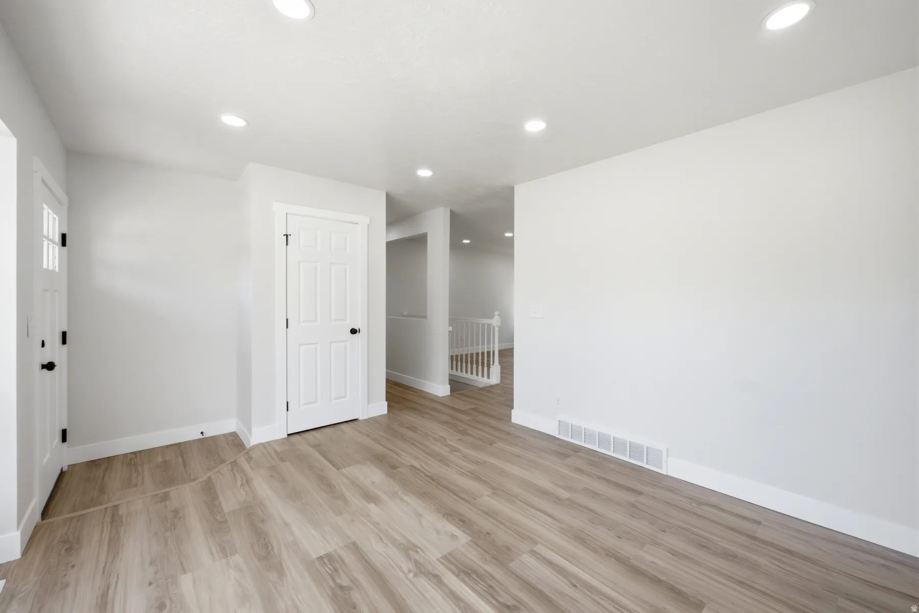 Open living space featuring recessed lighting, wood-finish flooring, white baseboards, and a paneled interior door with black hardware