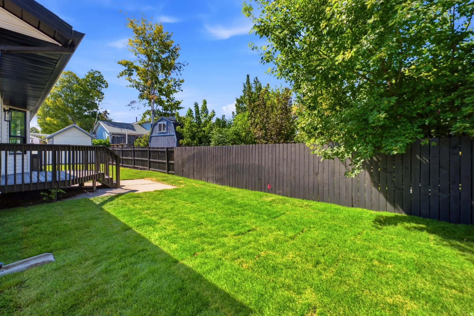Spacious backyard featuring a manicured lawn, a dark-stained privacy fence, and mature trees providing natural shading