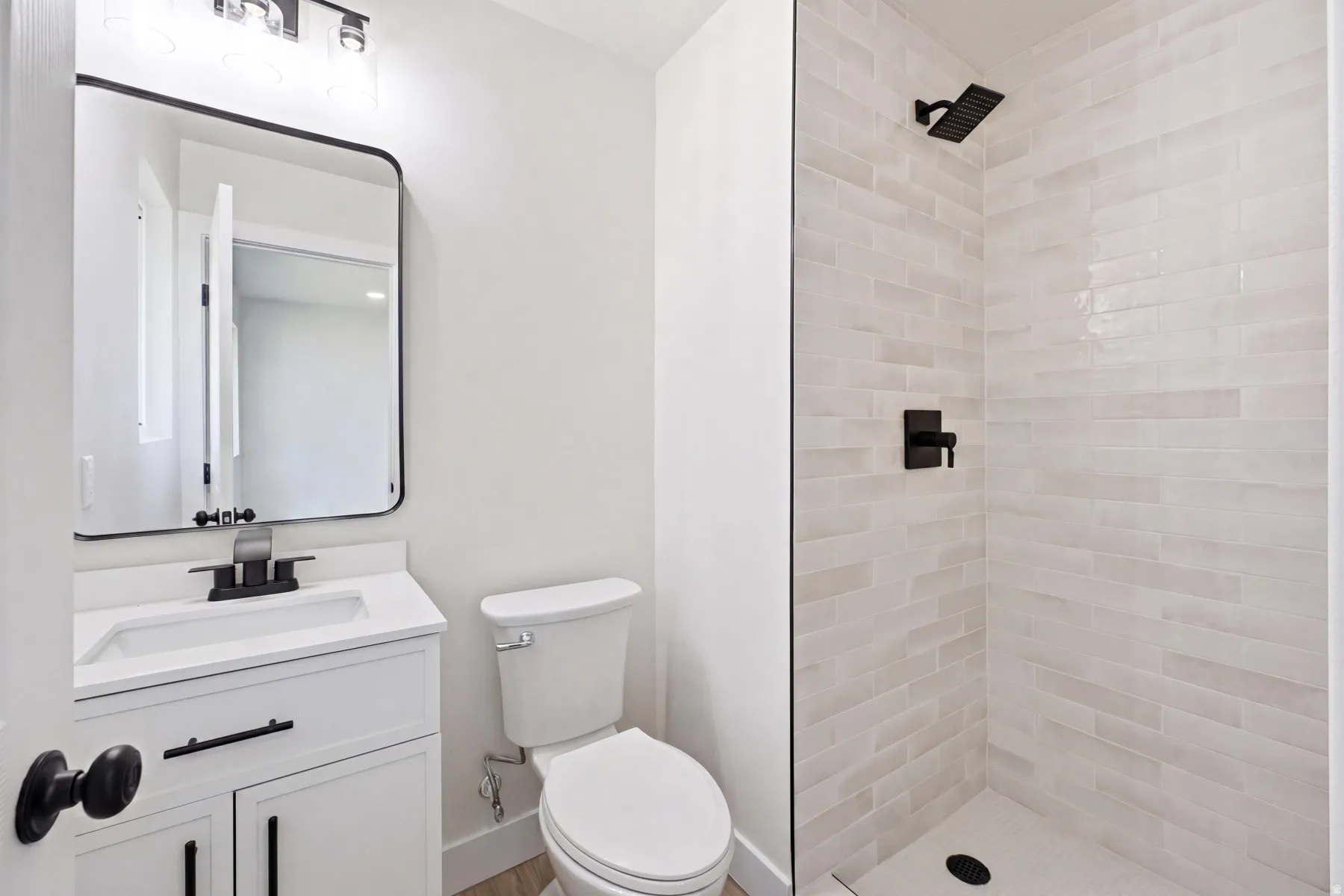 Bathroom featuring a white vanity with integrated sink, black hardware, framed mirror, and a walk-in shower with light-toned horizontal tile