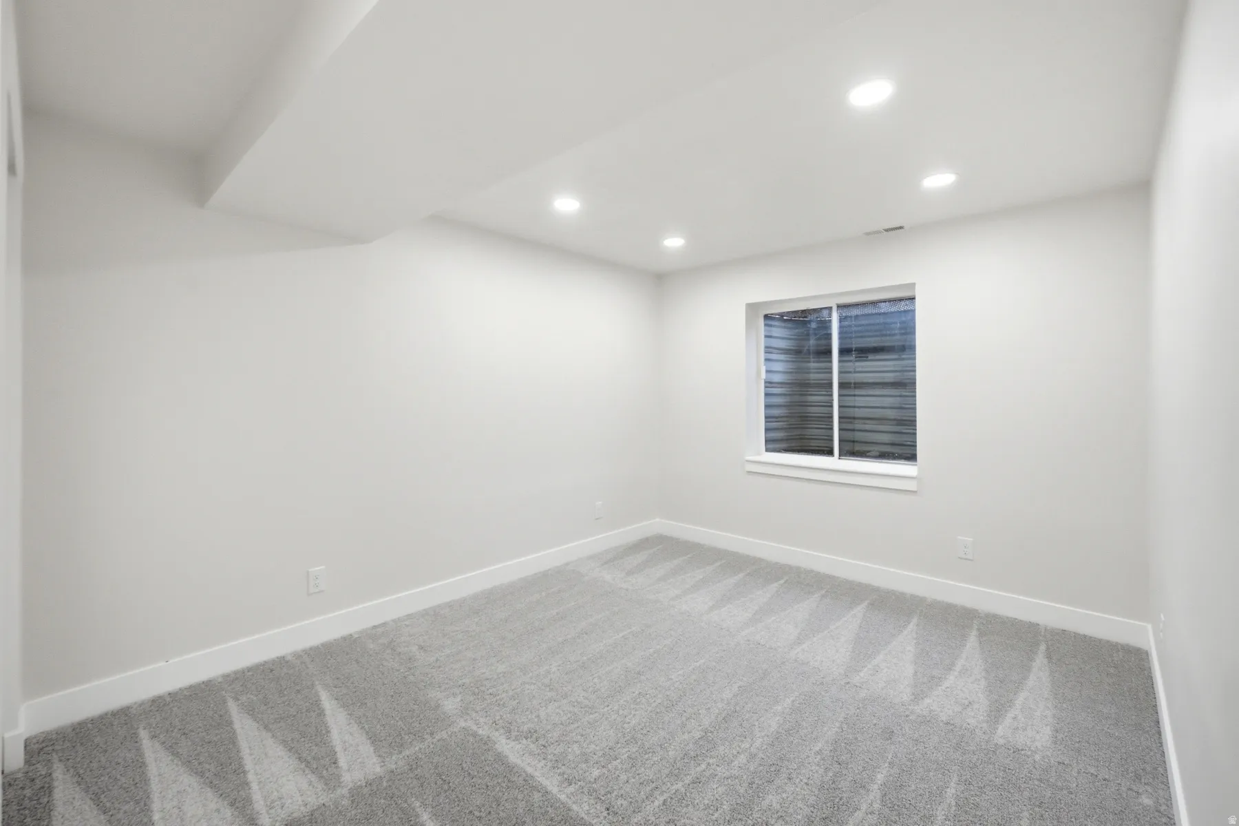 Recessed lighting illuminates this room featuring light grey walls and patterned carpeting
