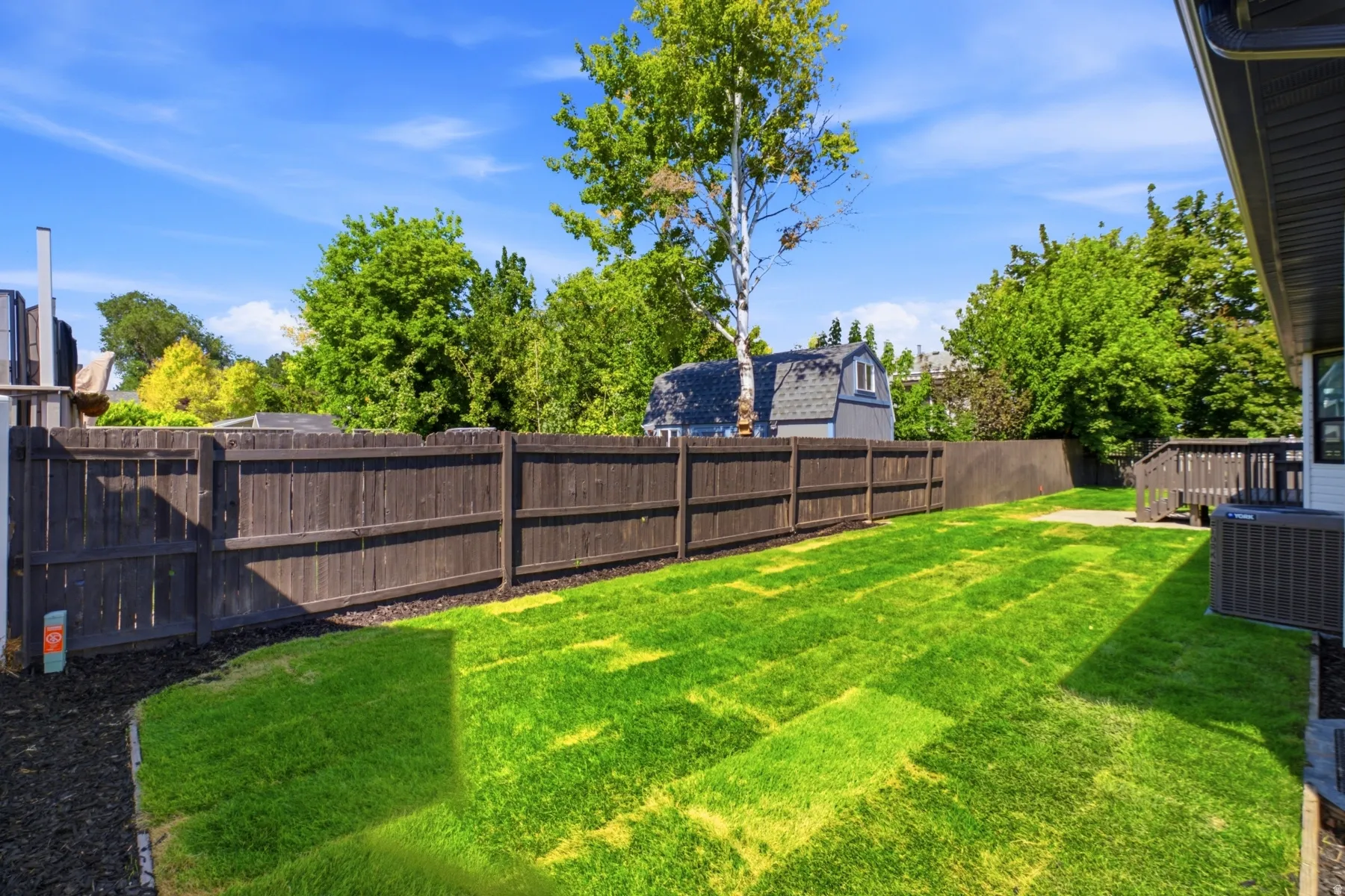 Expansive backyard featuring a manicured lawn, full privacy fencing, and a raised wooden deck with stairs