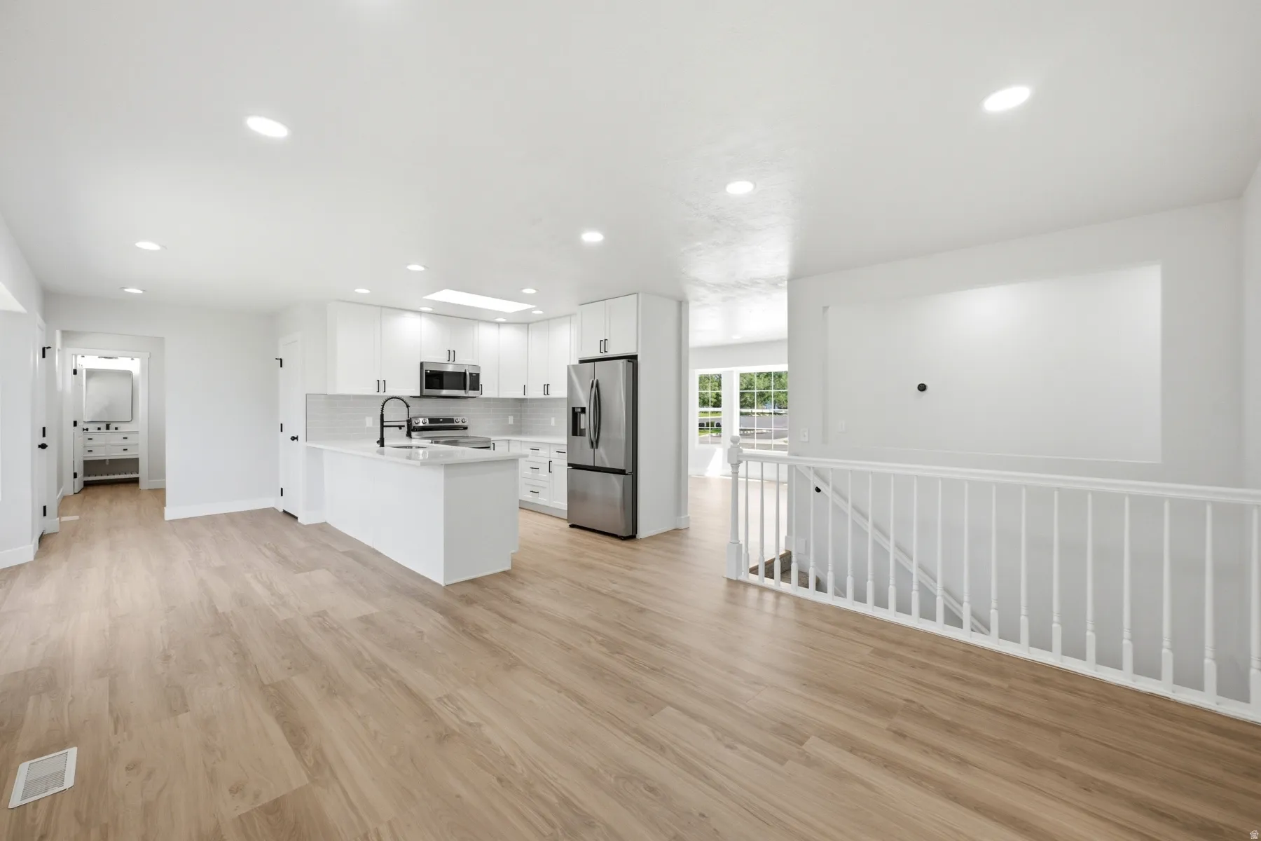 Open-concept living space featuring wood-finish flooring, recessed lighting, and a white kitchen with stainless steel appliances