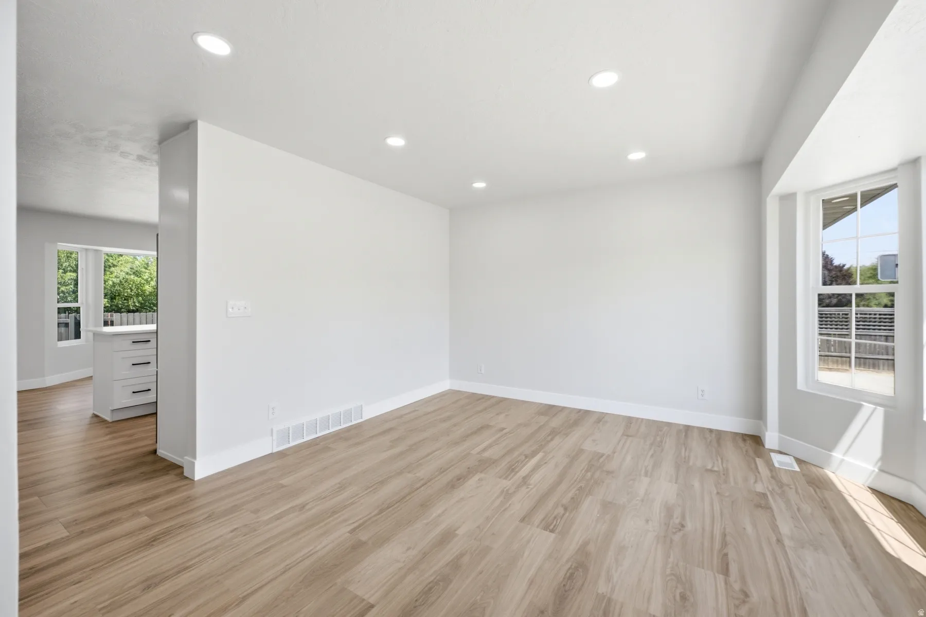 Open-concept living space featuring wood-finish flooring, recessed lighting, white baseboards, and a bay window