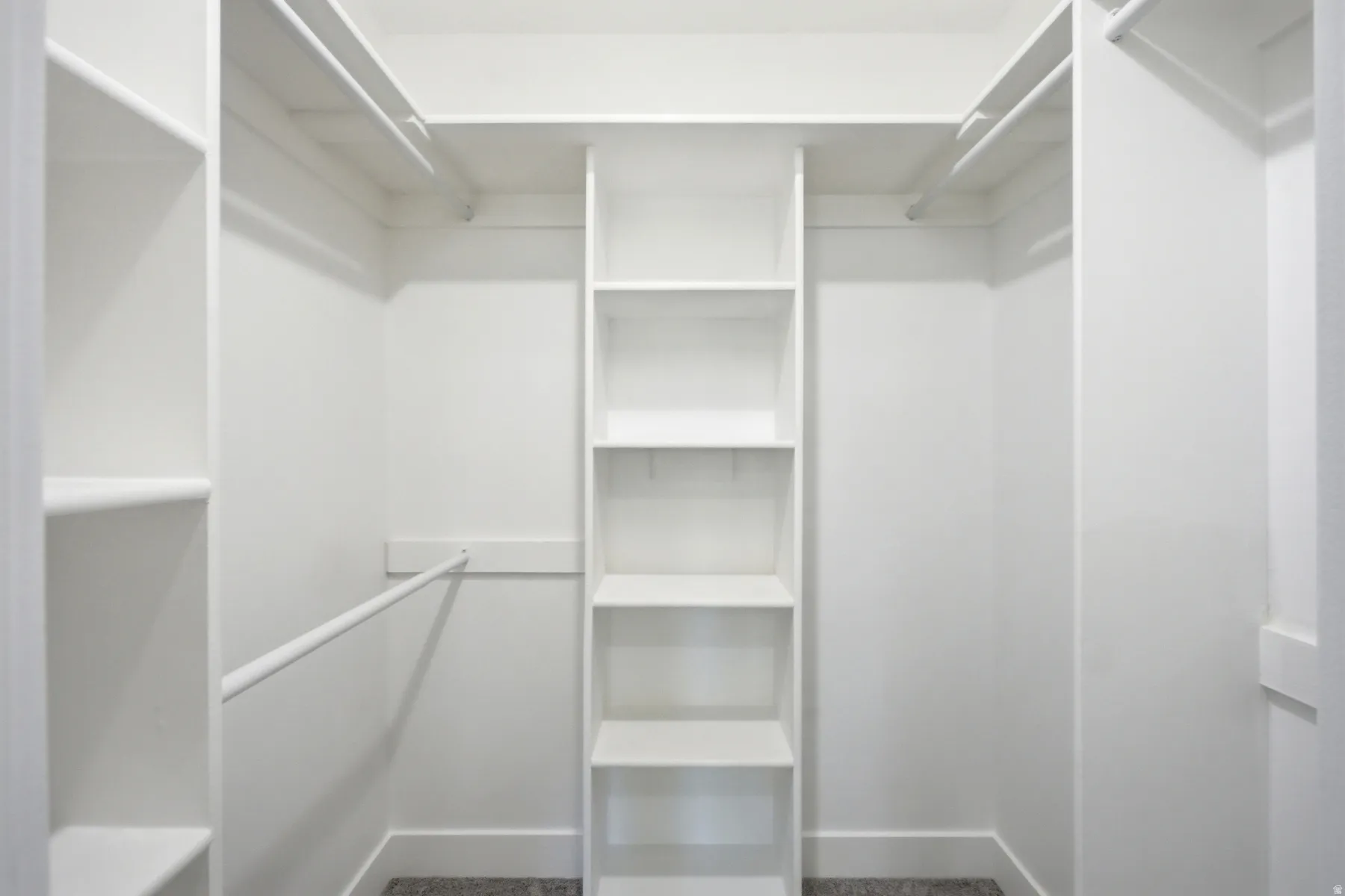 Spacious walk-in closet featuring white built-in shelving, multiple hanging rods, and light gray carpeting